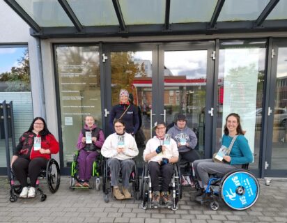 Hier sieht man die Erlanger Bildungsfachkräfte alle in Rollstühlen vor einer Eingangstür